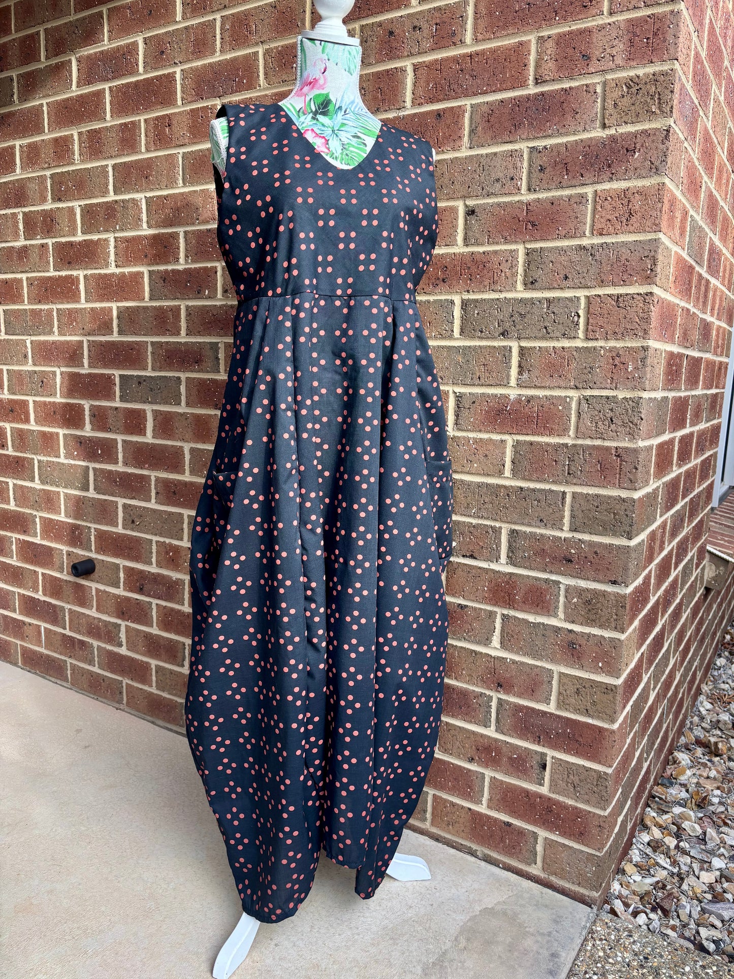 Black dress with red spots pattern on a mannequin against a brick wall.