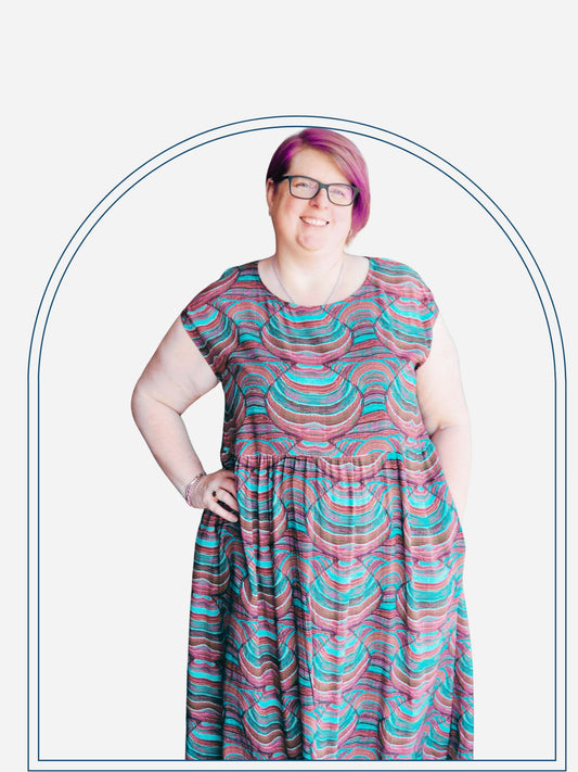A woman standing on a deck wearing a red and black geometric patterned cap-sleeve mid-length dress.