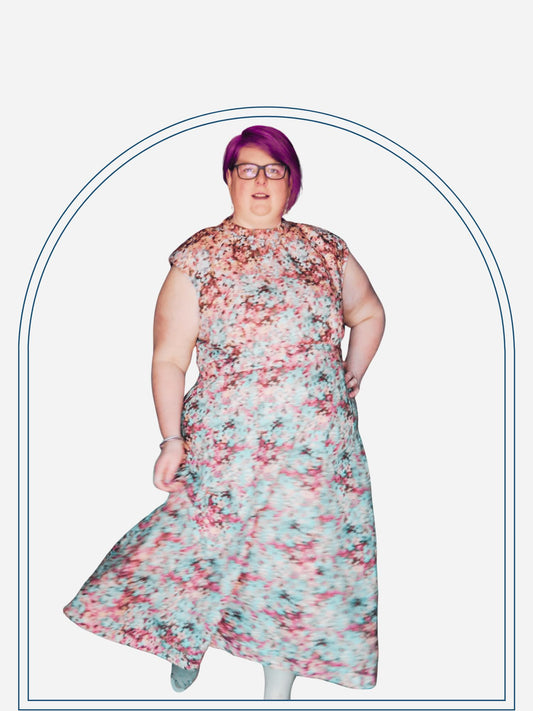 A woman wearing a floral print dress with three-quarter sleeves and a maxi skirt, standing in a doorway.