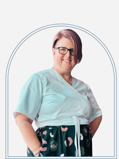 Person wearing a white top and patterned navy pants standing against a brick wall.