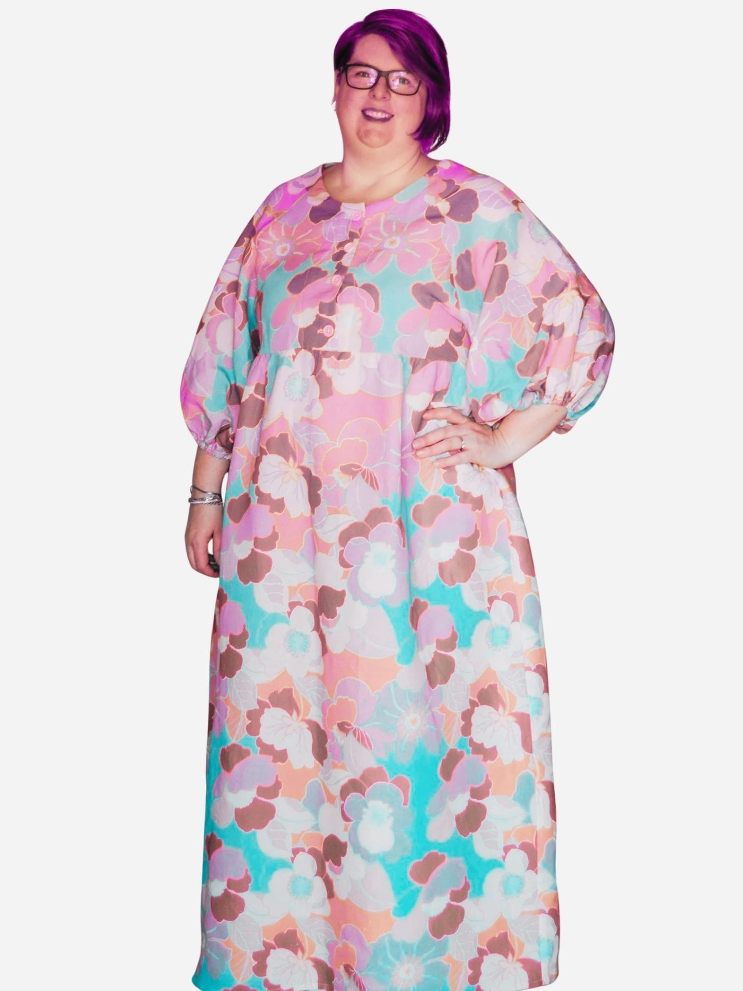 A woman standing in a colorful floral sleeve dress with pockets, posing against a modern art background.