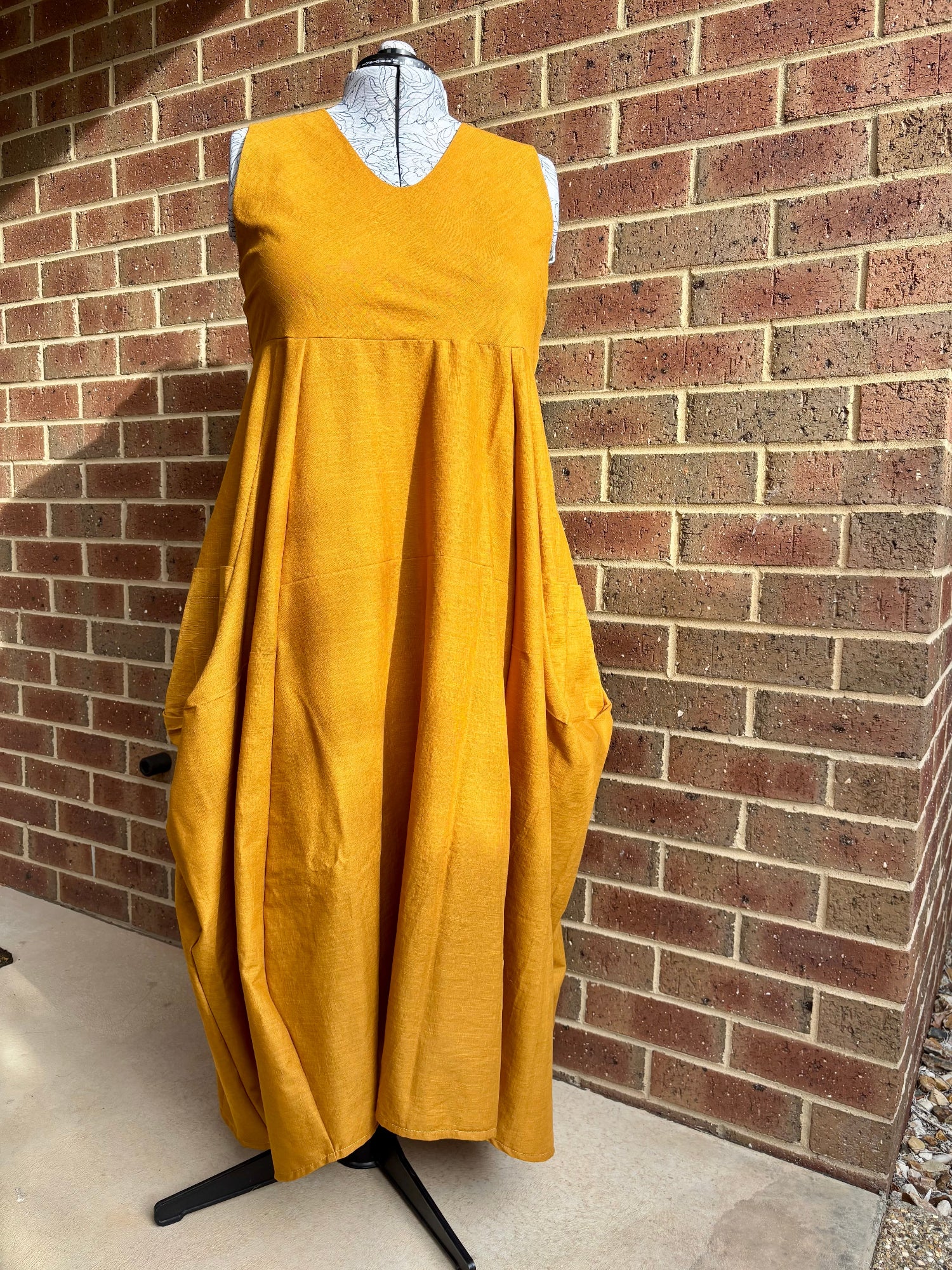 Mustard dress on a mannequin against a brick wall.