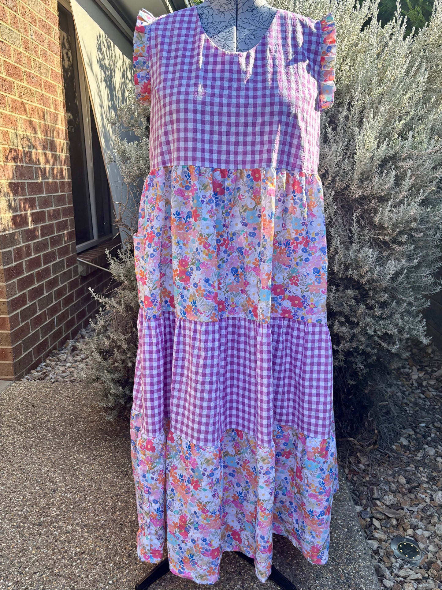 A floral tiered dress displayed on a mannequin, with pockets, against an outdoor background.
