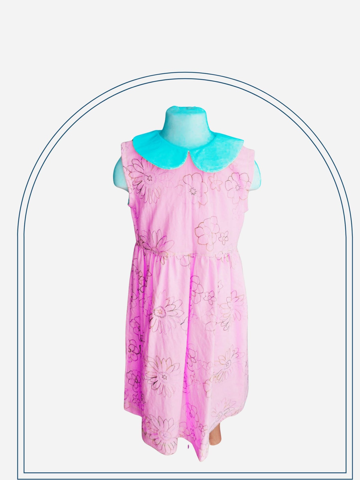 A yellow kids' dress with a lined bodice and sleeveless design, displayed on a mannequin, featuring a leaf pattern and a white collar with a ruffled edge.